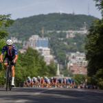 Ciclista em prova de estrada em Montreal com pelotão ao fundo