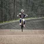 Ciclista de BMX salta sobre uma pista de terra durante uma manobra.