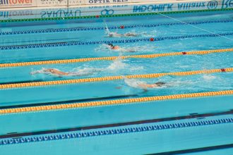Nadadores disputam uma prova em piscina, avançando lado a lado pelas raias.