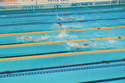Nadadores disputam uma prova em piscina, avançando lado a lado pelas raias.