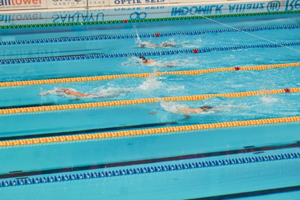 Nadadores disputam uma prova em piscina, avançando lado a lado pelas raias.