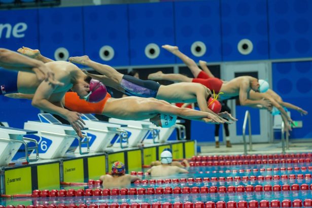Nadadores mergulham simultaneamente na piscina durante a largada de uma competição.