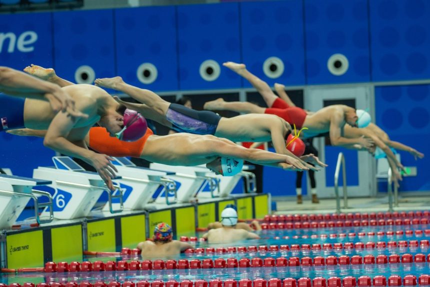 Nadadores mergulham simultaneamente na piscina durante a largada de uma competição.