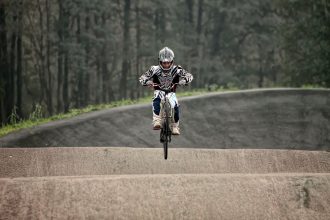 Ciclista de BMX salta sobre uma pista de terra durante uma manobra.