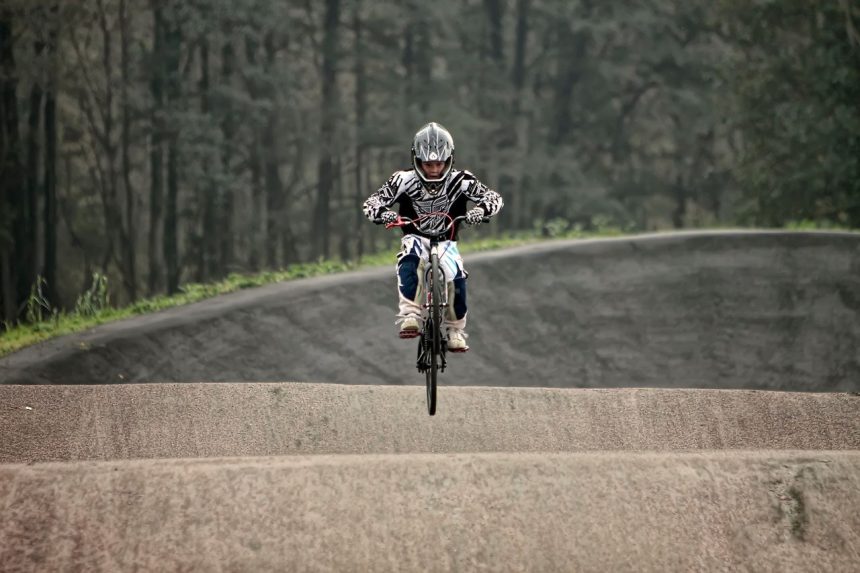 Ciclista de BMX salta sobre uma pista de terra durante uma manobra.