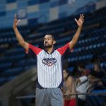 Árbitro sinaliza durante uma partida de basquete em uma arena coberta.