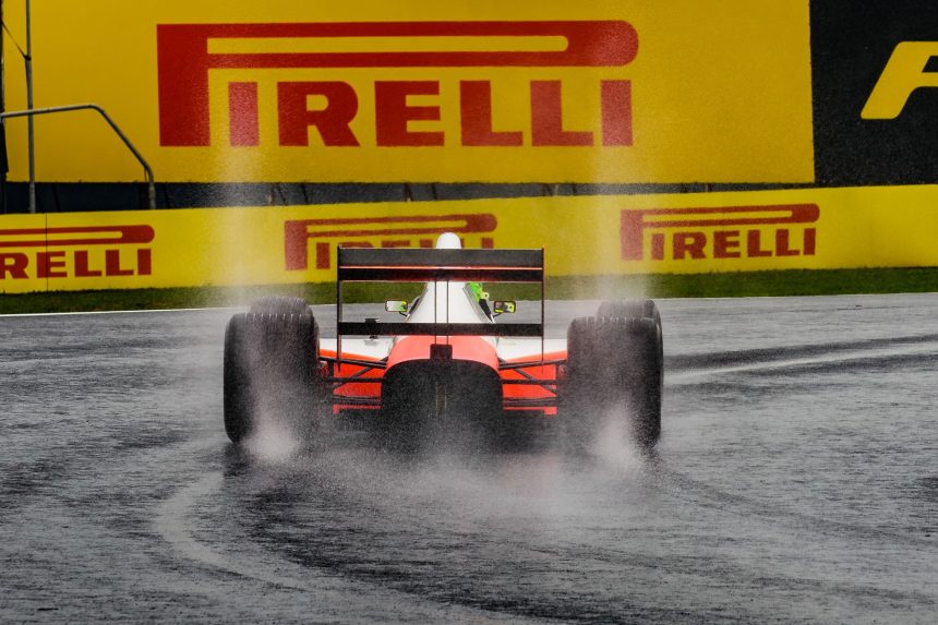 Carro de Fórmula 1 atravessa uma pista molhada, levantando spray sob uma placa da Pirelli.